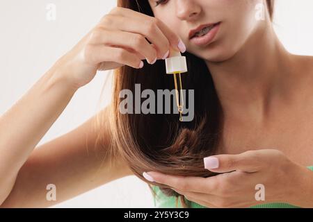 femme appliquant l'huile et le sérum sur les cheveux avec la pipette gros plan, sur fond blanc, concept de soins capillaires, cheveux sains Banque D'Images