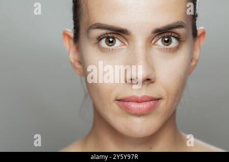 Cette image haute résolution capture les détails subtils du visage d'une jeune femme, montrant son expression calme et contemplative sur un b gris neutre Banque D'Images