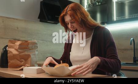 Surpris heureux heureux excité femme caucasienne client femme acheteur fille commande ouverte savoureux burger boîte en carton cheeseburger hamburger dame profiter Banque D'Images