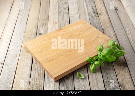 Planche à découper et basilic sur une vieille table de cuisine en bois. Fond culinaire. Planche à découper en bois vide, espace d'affichage du produit. Banque D'Images