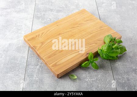 Planche à découper et basilic sur une table de cuisine grise. Fond culinaire. Planche à découper en bois vide, espace d'affichage du produit. Banque D'Images