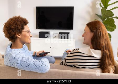 Regardant la télévision, deux amies femmes assis sur le canapé et parlant dans le salon Banque D'Images