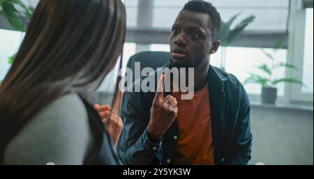 L'homme afro-américain agressif perd son sang-froid, commence à se battre, crie sur sa petite amie bouleversée pendant la thérapie de couple. Couple multiethnique en conflit en séance de conseil avec psychothérapeute familial. Banque D'Images