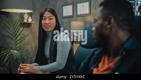 La petite amie asiatique en colère commence à se battre, crie à son petit ami. L'homme afro-américain nerveux perd son sang-froid, puis boit de l'eau. Couple multiethnique en conflit au cours d'une thérapie de couple avec psychologue. Banque D'Images