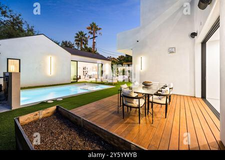 Jardin moderne doté d'une piscine, d'une terrasse en bois et d'un coin repas extérieur dans un cadre contemporain. Banque D'Images