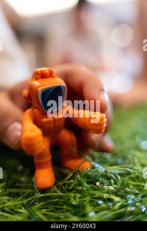 singe robot jouet orange sur herbe verte bébé main attrapant Banque D'Images