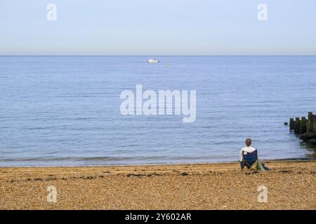 Whitstable, Kent, Angleterre, Royaume-Uni. Femme solitaire assise sur la plage regardant la mer Banque D'Images