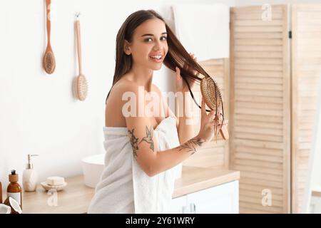 Belle jeune femme se brossant les cheveux avec de l'huile de noix de coco dans la salle de bain Banque D'Images