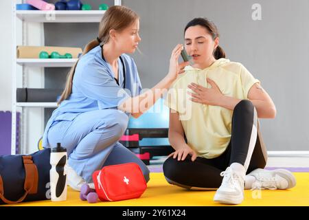 Médecin féminin avec inhalateur donnant les premiers soins à la jeune femme dans le gymnase Banque D'Images