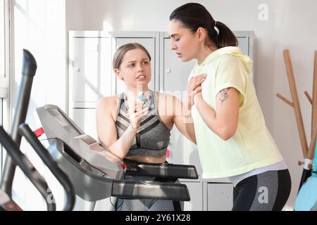 Entraîneur féminin donnant l'inhalateur à la femme avec la crise d'asthme sur tapis roulant dans le gymnase Banque D'Images