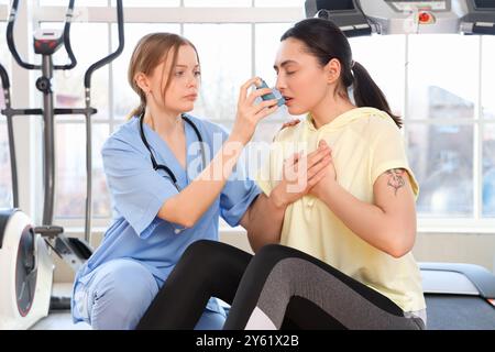 Médecin féminin avec inhalateur donnant les premiers soins à la jeune femme dans le gymnase Banque D'Images