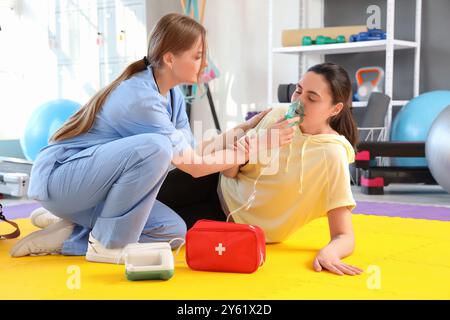 Médecin féminin avec nébuliseur donnant les premiers soins à la jeune femme dans le gymnase Banque D'Images