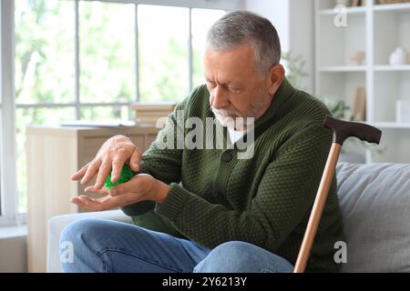 Homme âgé atteint du syndrome de Parkinson avec boule de massage à domicile Banque D'Images