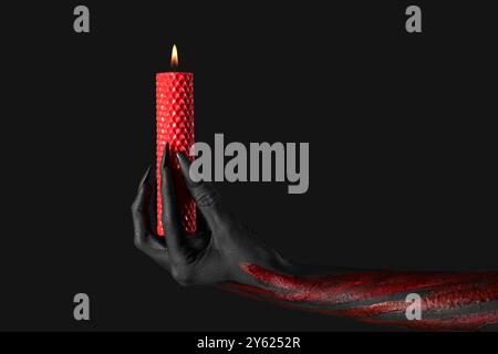 Main de sorcière sanglante avec griffes et bougie de cire brûlante sur fond noir. Célébration d'Halloween Banque D'Images