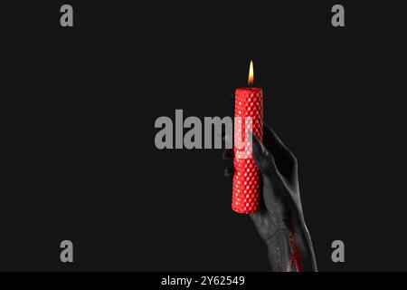 Main de sorcière sanglante avec griffes et bougie de cire brûlante sur fond noir. Célébration d'Halloween Banque D'Images