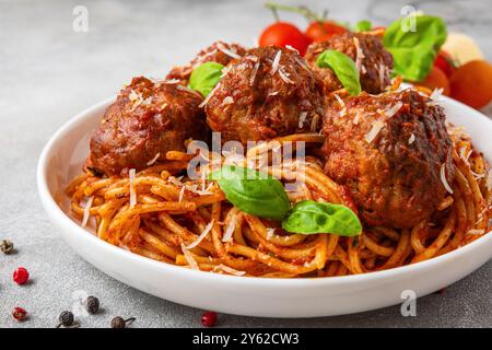 Spaghetti aux boulettes de viande dans une sauce tomate, garni de parmesan et de feuilles de basilic frais dans une assiette. Délicieuse cuisine italienne. Gros plan Banque D'Images