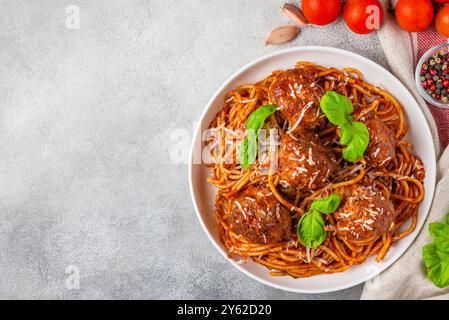 Spaghetti aux boulettes de viande dans une sauce tomate, garni de parmesan et de feuilles de basilic frais dans une assiette sur fond de béton gris. Délicieux Banque D'Images