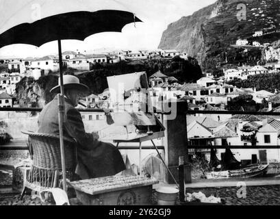 Portant chapeau et pardessus avec l'inévitable cigare en place M. WinstonChurchill qui est en vacances avec sa femme ici, est assis à peindre une scène du village de Camara de Lobos, près de Funchal, Madère. 9 janvier 1950 Banque D'Images