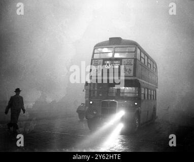 Une couverture de brouillard qui couvrait Londres amena le trafic routier et ferroviaire à une rampante et arrêta les navires et les avions. De nombreux passagers dans les véhicules publics ont dû marcher et, dans certains cas, ont aidé les conducteurs le long en marchant devant avec des torches allumées et des balises. Image montre : Un bus bien guidé par ses phares antibrouillard rampant le long du remblai dans le black-out . 6 décembre 1952 Banque D'Images