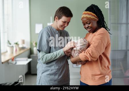 Infirmière vérifiant sur le nouveau-né pendant que la mère tient le nourrisson près dans la chambre d'hôpital en souriant mère s'engageant avec l'infirmière et le bébé Banque D'Images