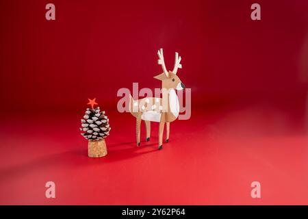 Présentoir festif de vacances sur fond rouge avec artisanat de papier de recyclage, sapin de Noël en pomme de pin plus une figurine de renne en carton avec tache blanche Banque D'Images