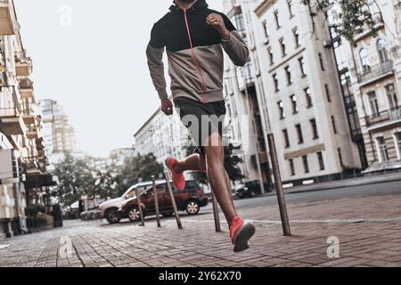 Sur le chemin de la grande forme. Gros plan d'un jeune homme en vêtements de sport courant le long de la rue de la ville Banque D'Images