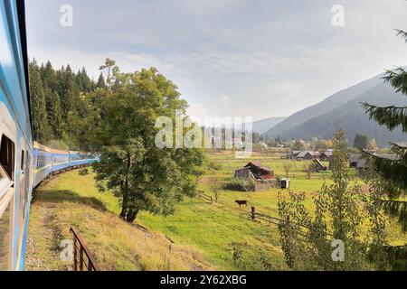 Vue depuis la fenêtre du train au village ensoleillé. Carpates, Ukraine Banque D'Images
