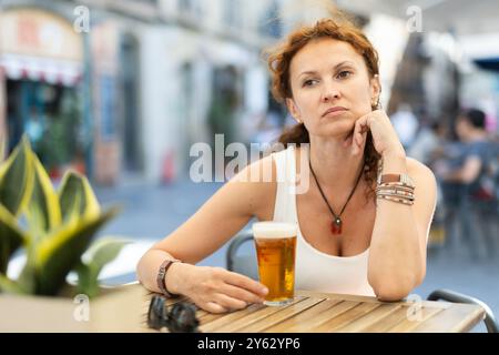 Femme d'âge mûr réfléchie buvant de la bière dans un café en plein air Banque D'Images