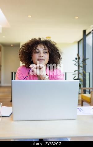 Travailler sur ordinateur portable, femme en chemise rose pensant et tenant un stylo, espace de copie, à la maison Banque D'Images