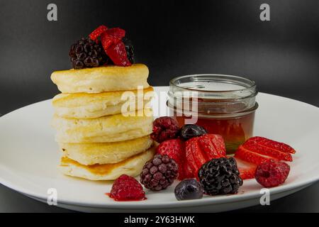 Savoureuses crêpes végétaliennes, végétariennes sans produits laitiers au beurre avec des baies recouvertes, sirop d'érable sur une assiette blanche avec fond noir. Banque D'Images