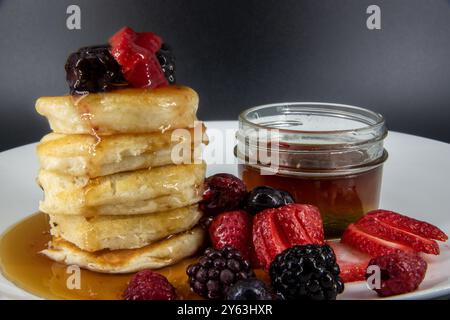 Savoureuses crêpes végétaliennes, végétariennes sans produits laitiers au beurre avec des baies recouvertes, sirop d'érable sur une assiette blanche avec fond noir. Banque D'Images