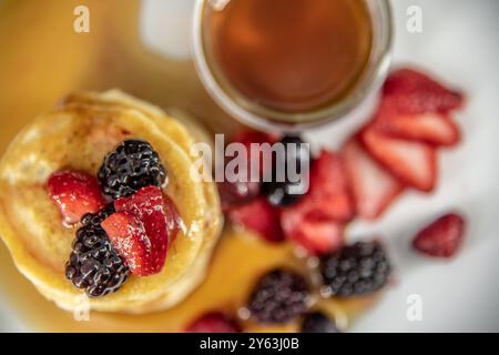 Savoureuses crêpes végétaliennes, végétariennes sans produits laitiers au beurre avec des baies recouvertes, sirop d'érable sur une assiette blanche avec un fond Uni. Banque D'Images