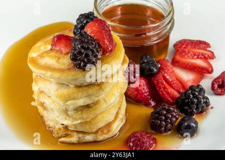 Savoureuses crêpes végétaliennes, végétariennes sans produits laitiers au beurre avec des baies recouvertes, sirop d'érable sur une assiette blanche avec un fond Uni. Banque D'Images