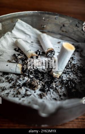 Cigarettes brûlées dans un cendrier sur une table en bois avec du papier mouillé à l'intérieur Banque D'Images