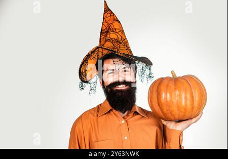 Ingrédients de cuisine saisonniers de Thanksgiving. Bel homme d'Halloween avec citrouille à la main. Autocollants Halloween joyeux. Homme barbu d'Halloween dans le chapeau de sorcière - Banque D'Images