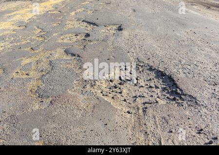 Mauvaise route, asphalte fissuré avec nids de poule et gros trous. Nids de poule sur la route avec des pierres sur l'asphalte. La surface asphaltée est détruite sur la route. Banque D'Images