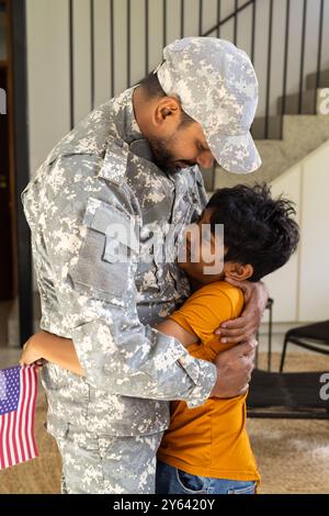 Père indien militaire en uniforme embrassant son jeune fils tenant le drapeau américain à l'intérieur Banque D'Images