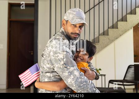 Père indien militaire en uniforme embrassant son jeune fils tenant le drapeau américain à l'intérieur Banque D'Images