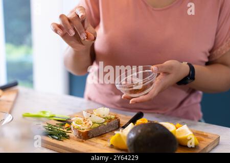 Ajouter un assaisonnement à un toast à l'avocat sain, femme préparant dans la cuisine, à la maison, à la maison Banque D'Images