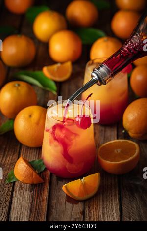 Cocktail classique de tequila au lever du soleil, superposé de tequila aux teintes vibrantes de jus d'orange et de grenadine, garni d'une brochette de cerises maraschino. La grenadine est po Banque D'Images