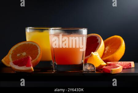 Verres de pamplemousse et jus d'orange avec de la glace sur un fond noir. Boissons rafraîchissantes avec des tranches de fruits. Banque D'Images