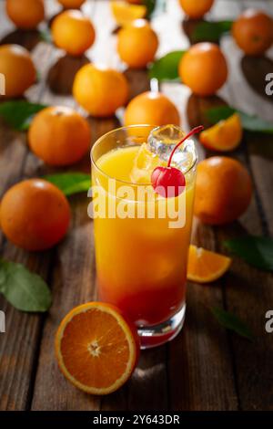 Cocktail classique de tequila au lever du soleil, superposé de tequila aux teintes vibrantes de jus d'orange et de grenadine, garni d'une brochette de cerises maraschino. Banque D'Images