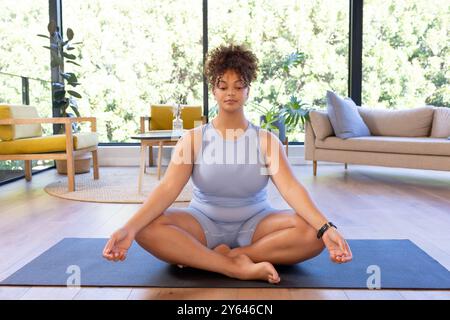 Méditer sur le tapis de yoga, femme de taille plus pratiquant la pleine conscience à la maison, à la maison Banque D'Images