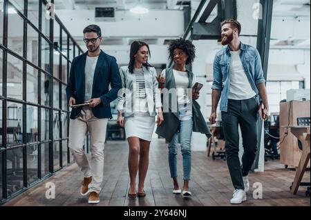 Dans l'attente de leur prochaine réunion. Toute la longueur des jeunes gens modernes dans les vêtements décontractés intelligents discutant des affaires tout en marchant à travers le bureau co Banque D'Images