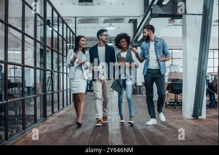 Des affaires créatives en déplacement. Toute la longueur des jeunes collègues dans le style décontracté élégant marcher et parler pendant une pause café au travail Banque D'Images