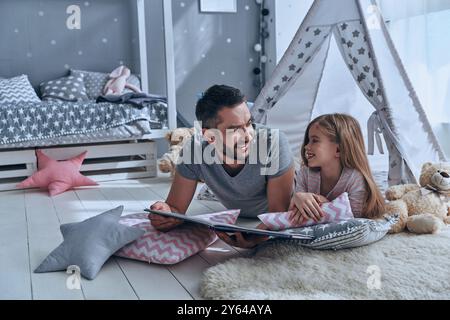 Passer du temps sans soucis. Père et fille se regardant l'un l'autre tout en étant couchés sur le sol dans la chambre Banque D'Images