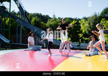 Familles heureuses avec des enfants jouant et s'amusant sur une surface gonflable dans un terrain de jeux extérieur animé par une journée ensoleillée. Une joyeuse scène de rire et Banque D'Images