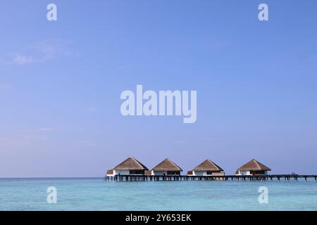 Une vue sereine de bungalows sur pilotis dans une mer turquoise claire sous un ciel bleu vif. La scène transmet la tranquillité et le paradis tropical. Banque D'Images