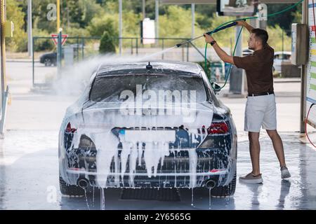 L'homme lave la mousse de la voiture avec de l'eau sous haute pression Banque D'Images