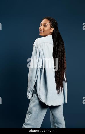 Une jeune femme confiante pose de manière ludique dans une tenue en denim tendance, mettant en valeur ses longs cheveux. Banque D'Images